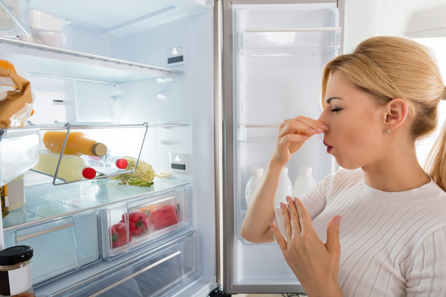 a woman opened refrigerator door and she put a hand on her nose because of the bad odor from refrigerator.