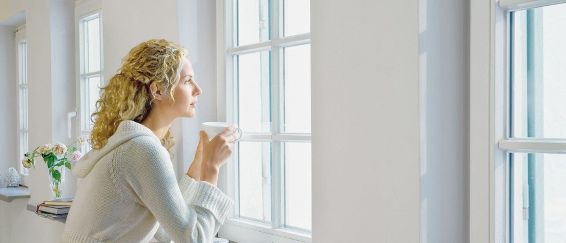 a woman looking outside the window with a cup of coffee in her hand, enjoying fresh indoor environment.
