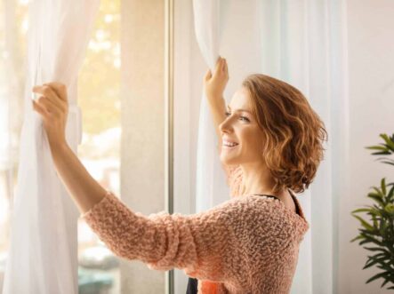 a woman opening curtains with a smiling face.