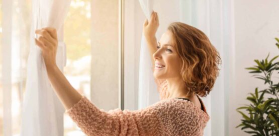 a woman opening curtains with a smiling face.