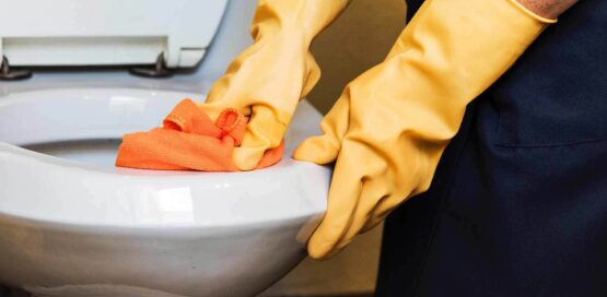 a person cleaning toilet seat wearing yellow gloves and cleaning toilet seat with orange color cloth.